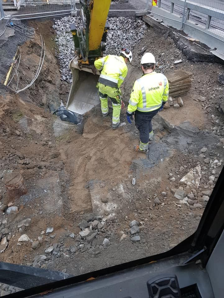 To menn i arbeidsklær ved gravemaskin